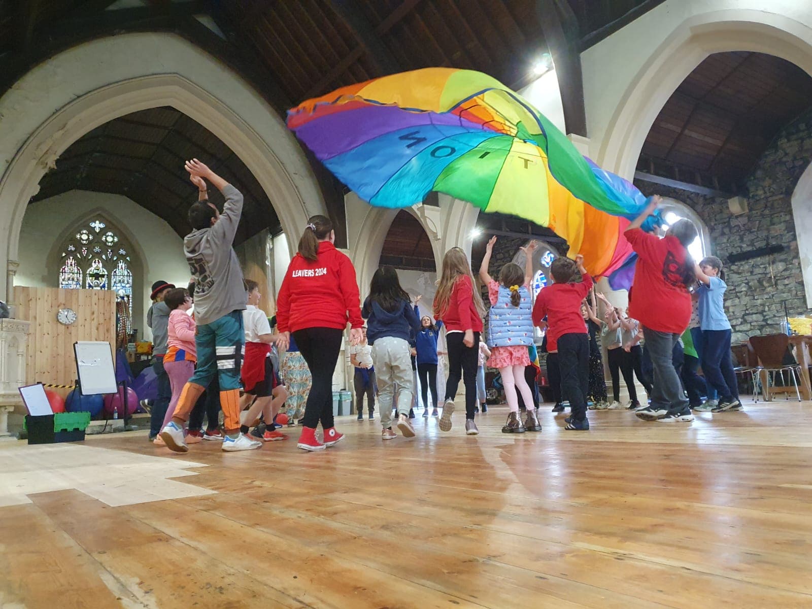 A photograph of a group of children playing with a colourful parachute inside an old church.