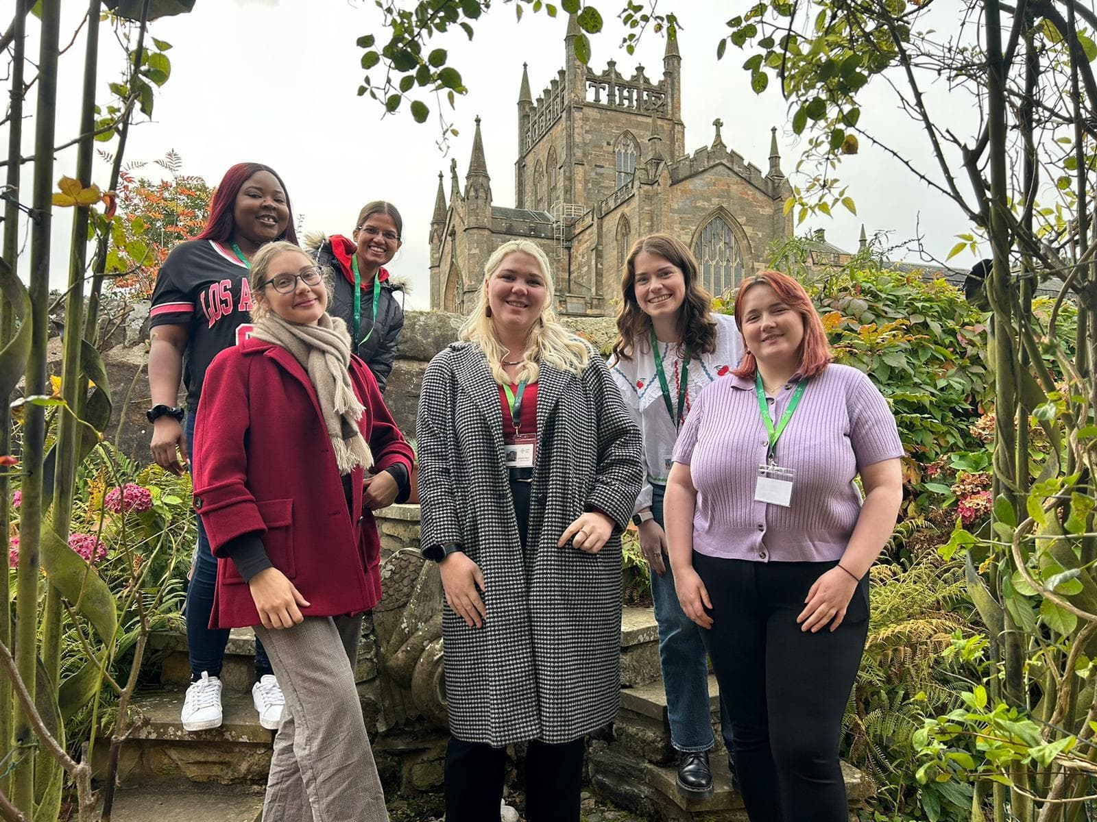 A group of six young women stand in a garden. Behind them is Dunfermline Abbey.